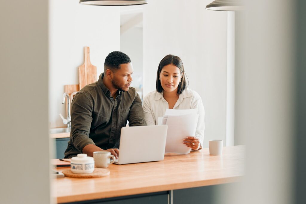 Couple with laptop looking at document, paper work or finances with confused expression for overdue